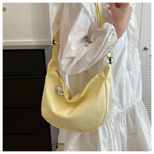 Close-up of yellow canvas crescent bag with plush charm and adjustable shoulder strap