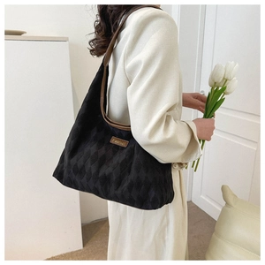 Detail of black quilted tote bag with brown leather trim and fashion patch on shoulder