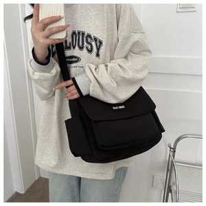 Detail of black canvas messenger bag featuring a brand logo tag and side pocket on person