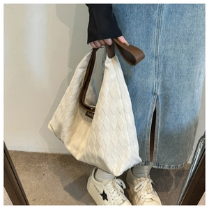 Detail of cream quilted tote bag with brown leather handles held by a model