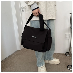Detail of black canvas messenger bag featuring a flap closure and DUO NING logo patch