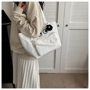 Detailed shot of white canvas tote bag with cartoon eyes and plush coal sprite charm