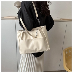 Detail view of cream white leather tote bag featuring dual front pockets and silver chain strap