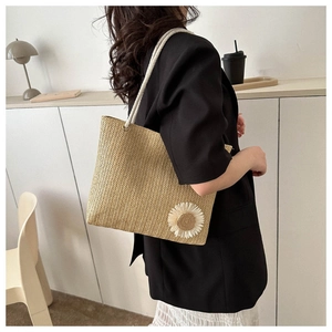 Detail of woven straw tote bag featuring a 3D daisy flower and white rope shoulder straps
