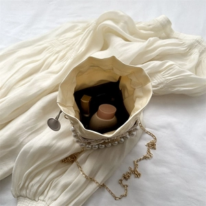Straw bucket bag with pearls and gold chain strap showing interior makeup storage space