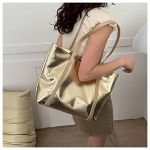 Detail of a large gold metallic tote bag worn over the shoulder by a model