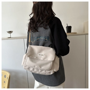 Detail of off-white canvas messenger bag with brand patch and adjustable shoulder strap