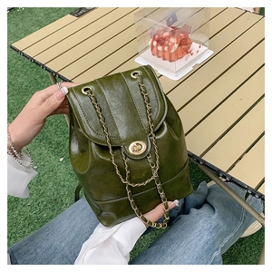Detail of dark green oil wax leather backpack with gold chain strap in outdoor setting