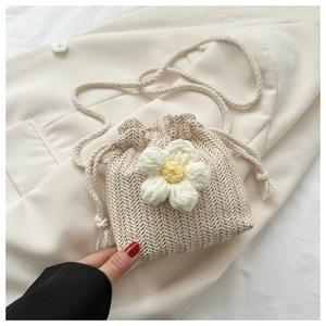 Detail of beige woven drawstring bucket bag featuring a handcrafted white crochet flower