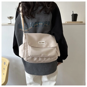 Detail of a beige canvas messenger bag showing the flap closure and brand woven label