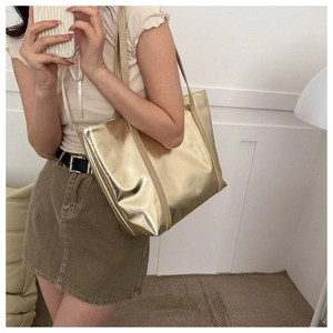 Detailed side view of large metallic gold tote bag carried by a model in a minimalist room
