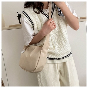 Close-up of a beige canvas half-moon crossbody bag with a cute pendant and wide strap