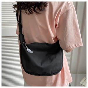 Detail of black half-moon canvas crossbody bag with cute cartoon charm on strap