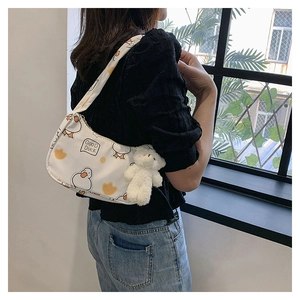 Close-up of white underarm bag with cartoon duck print and plush bear pendant detail