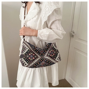 Ethnic woven hobo bag with colorful geometric patterns shown on a white lace dress