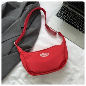 Detail view of a red nylon crescent crossbody bag with white fashion patch on white fabric
