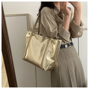 Detail of a large gold tote bag with a mirror finish worn with a khaki shirt dress
