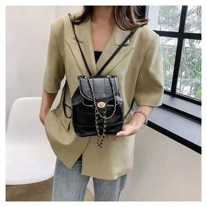 Detail of a chic black mini backpack with gold chain straps styled on a green blazer