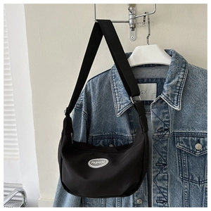 Detail of black nylon crescent shoulder bag with wide strap hanging near a denim jacket