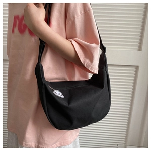 Side view of black canvas crescent bag with cute cartoon charm and adjustable strap