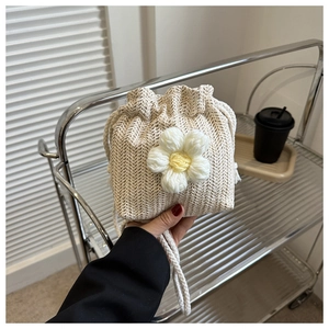 Detail of hand-woven cream bucket bag with large white knit daisy and drawstring