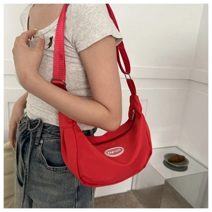 Detail of red crescent canvas crossbody bag showing adjustable strap and fashion label