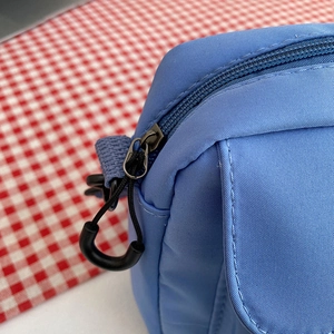 Sky blue nylon crossbody bag featuring top zipper closure with circular pull tab
