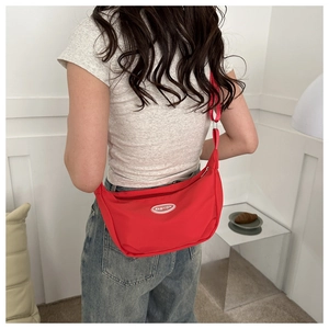 Detail of red crescent canvas bag with fashion logo worn as a crossbody by a model
