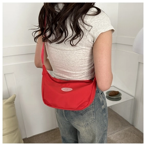 Back view of a red crescent canvas crossbody bag worn by a model in a minimalist setting