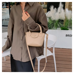 Minimalist beige pebble leather bucket bag with handle held by model on outdoor terrace