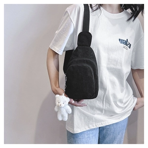 Close-up of black corduroy chest bag with a cute white plush bear pendant on a model