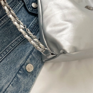 Metallic silver shoulder bag with braided chain strap on blue denim jacket backdrop