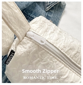 Detail of white wrinkled nylon bag featuring smooth zipper and fashion label on denim background
