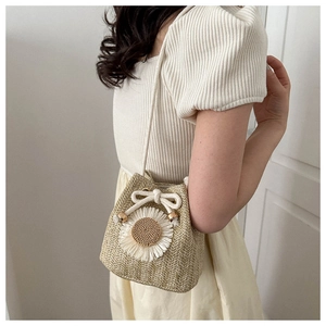 Straw bucket bag detail featuring large daisy floral accent and white drawstring closure