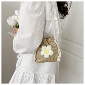 Detail of woven straw bucket bag featuring a white crochet flower and rope handle