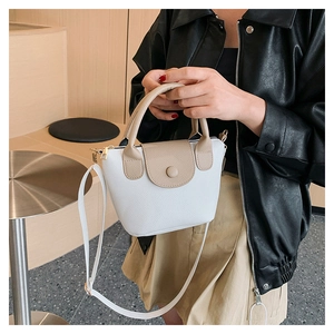 Detail of a white lychee grain bucket bag with brown contrast straps held by a model