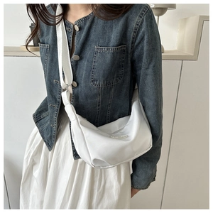 Close-up of white crescent canvas crossbody bag worn with denim jacket style