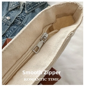 Close-up of smooth metal zipper closure on canvas tote bag with textured beige fabric