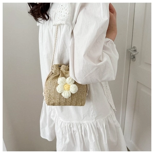 Mini straw bucket bag with white flower detail shown on a model in a white dress