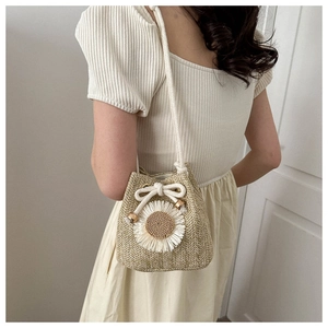 Detail of straw bucket bag with white flower decoration and drawstring on a model
