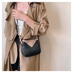 Detail of color-block bucket bag with gold trim worn with a khaki trench coat