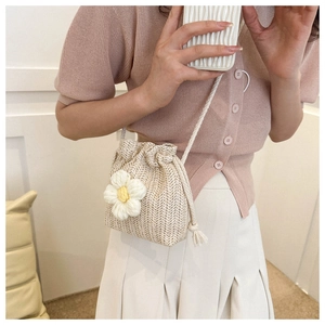 Detail of beige straw bucket bag featuring a knit flower and drawstring closure