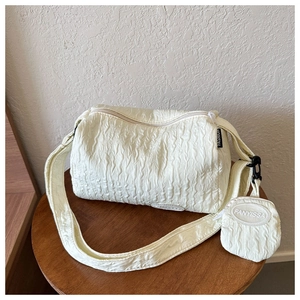Detail of creamy white pleated shoulder bag with mini coin purse on a wooden stool