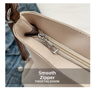 Detail shot of a smooth zipper closure on a cream canvas tote bag with brown leather strap