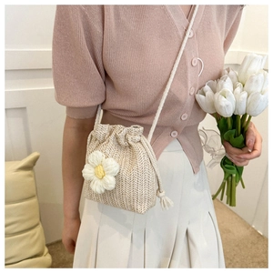 Chic beige woven drawstring bucket bag with a knit flower detail on a model in a soft setting