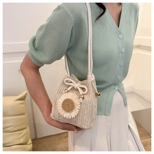 Detail of woven straw bucket bag with a white sunflower tassel and metal drawstring beads