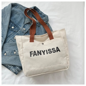 Detail of canvas tote bag with brown fabric handles and front pocket with snap closure