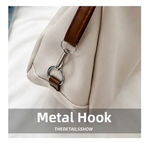 Close-up of silver metal swivel hook and brown leather trim on cream canvas bag