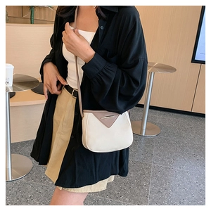 Close-up of a stylish cream and brown crossbody bag worn in a cozy cafe setting