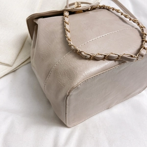 Chic beige bucket bag with gold chain strap and pebbled leather texture on white fabric